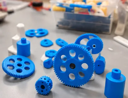 Close-up of blue 3D-printed gears, spacers, and small white parts spread across a gray work mat